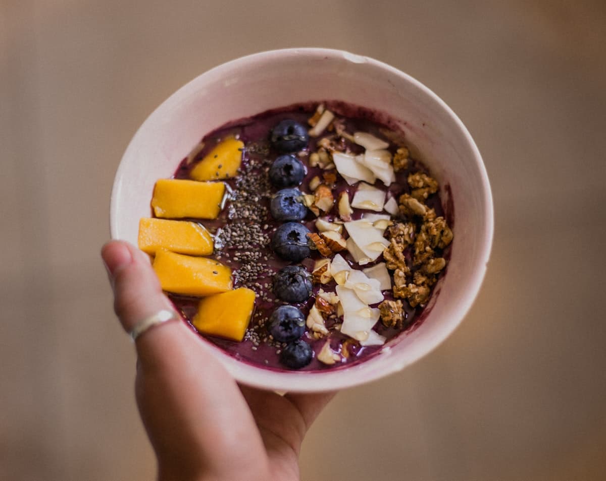 Manos sosteniendo un bowl de açaí con mango